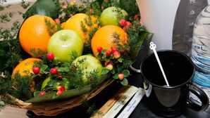 Eine Obstschale mit Orangen und Äpfeln, eine schwarze Tasse und eine Wasserflasche auf einem Tisch.