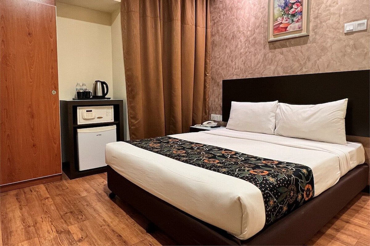 A hotel room with a large bed, a small desk with a coffee maker, a telephone, and a painting on the wall.