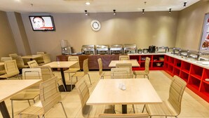 Ein Restaurant mit mehreren Tischen und Stühlen, einem Buffetbereich mit Speisenauslagen und einem wandmontierten Fernseher.