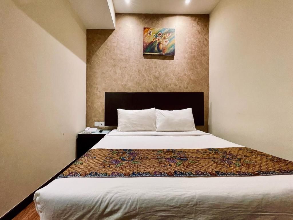 A hotel room with a large bed, a nightstand, a painting on the wall, and a patterned bedspread.