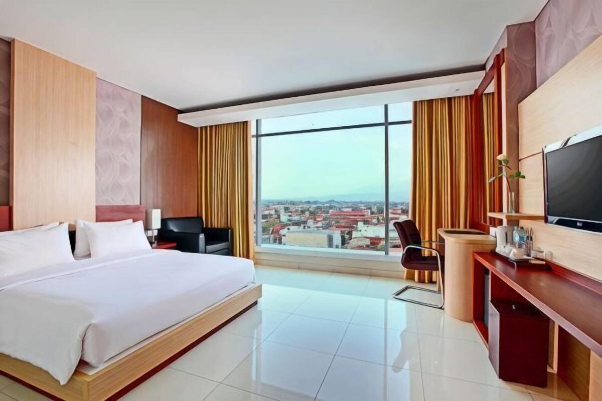 A hotel room with a large bed, a desk, a TV, and a view of the city.
