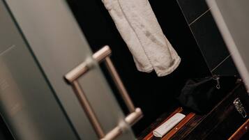 A white bathrobe hanging on a wooden hanger in a bathroom with black tiled walls and a wooden floor.