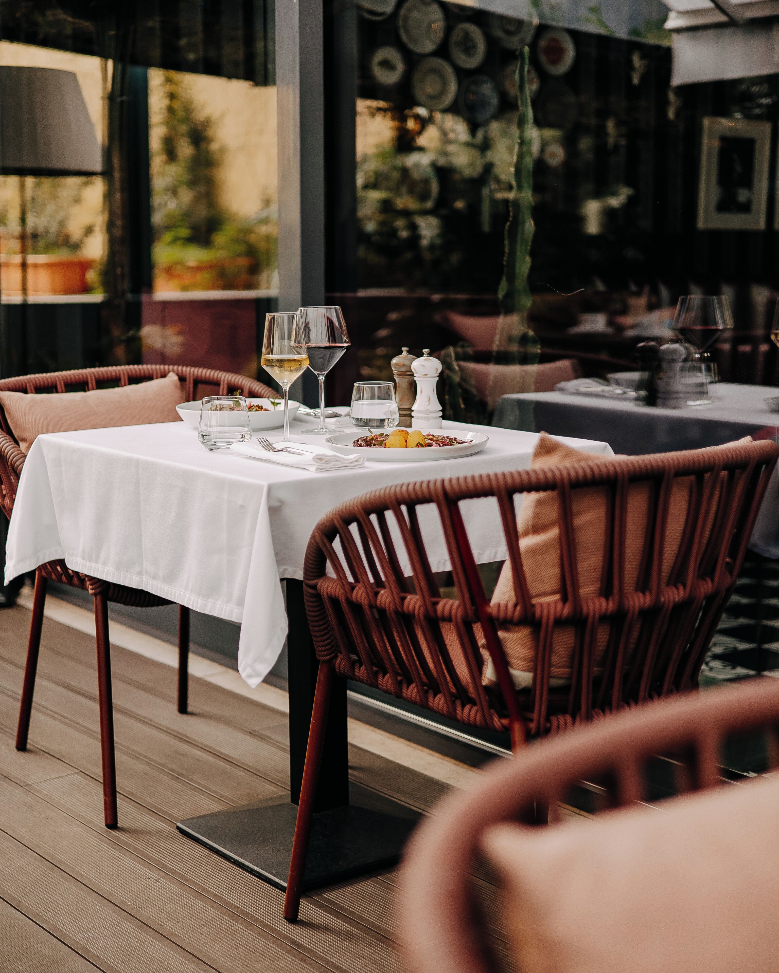 A dining table set with plates, glasses, and cutlery, surrounded by wicker chairs.