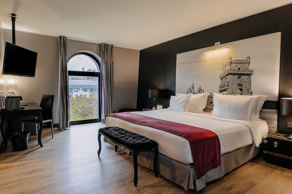 Ein modernes Hotelzimmer mit einem großen Bett, einem Schreibtisch, einer Bank und einem Fernseher.