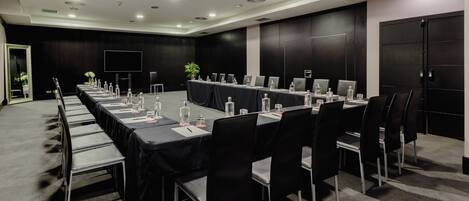 Un salón de conferencias con una larga mesa, sillas y computadoras portátiles.