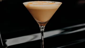 Un bicchiere da martini con schiuma sopra, appoggiato su un sottobicchiere rosso, su una superficie nera.