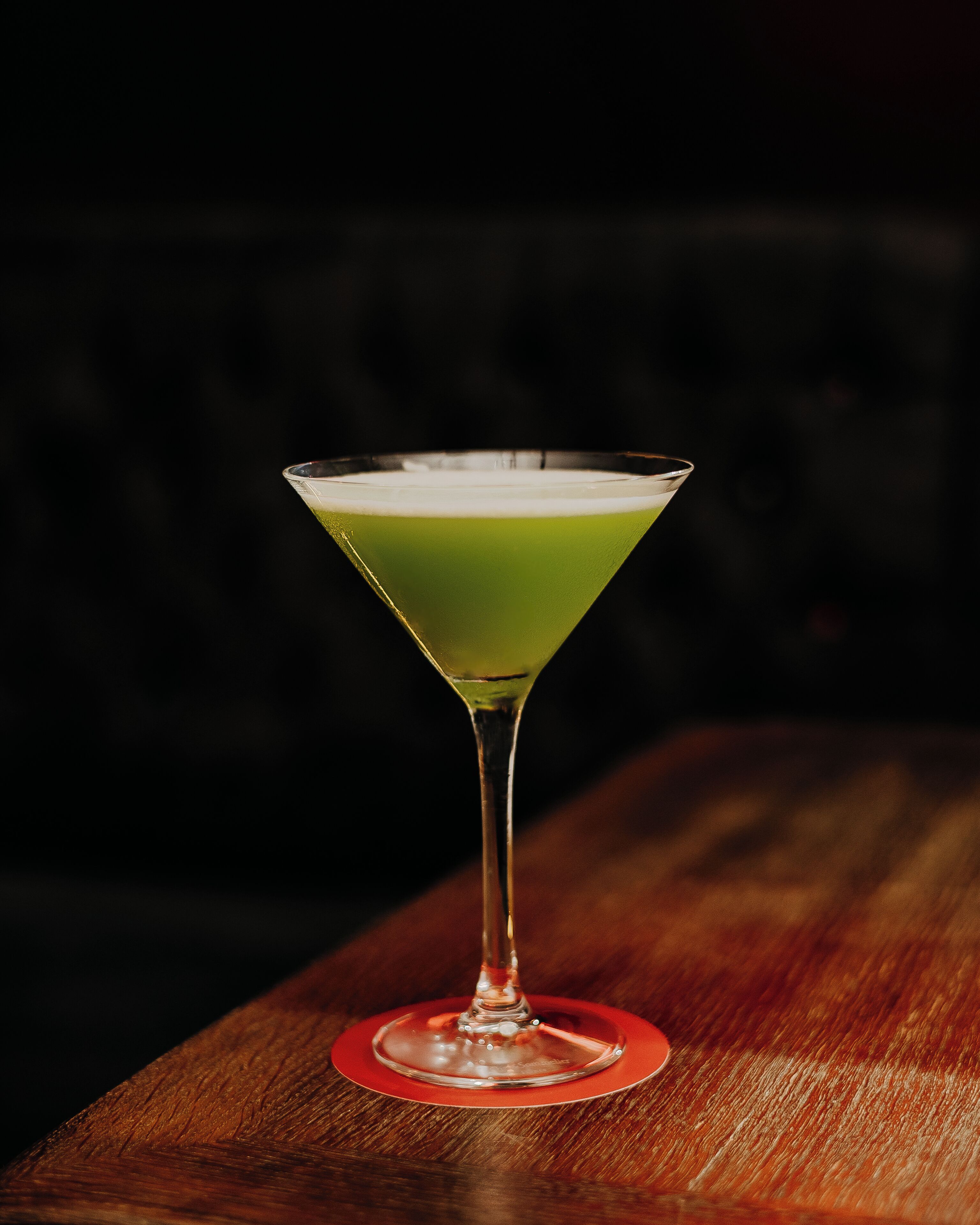 A martini glass with a green liquid on a wooden surface.