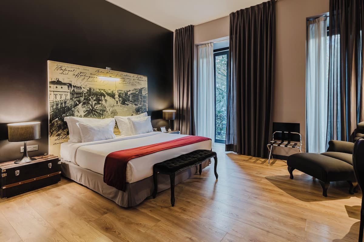 Ein Hotelzimmer mit einem großen Bett, einer Bank, einem Sessel, einem Nachttisch, einer Lampe und einer Wand mit einer historischen Karte.