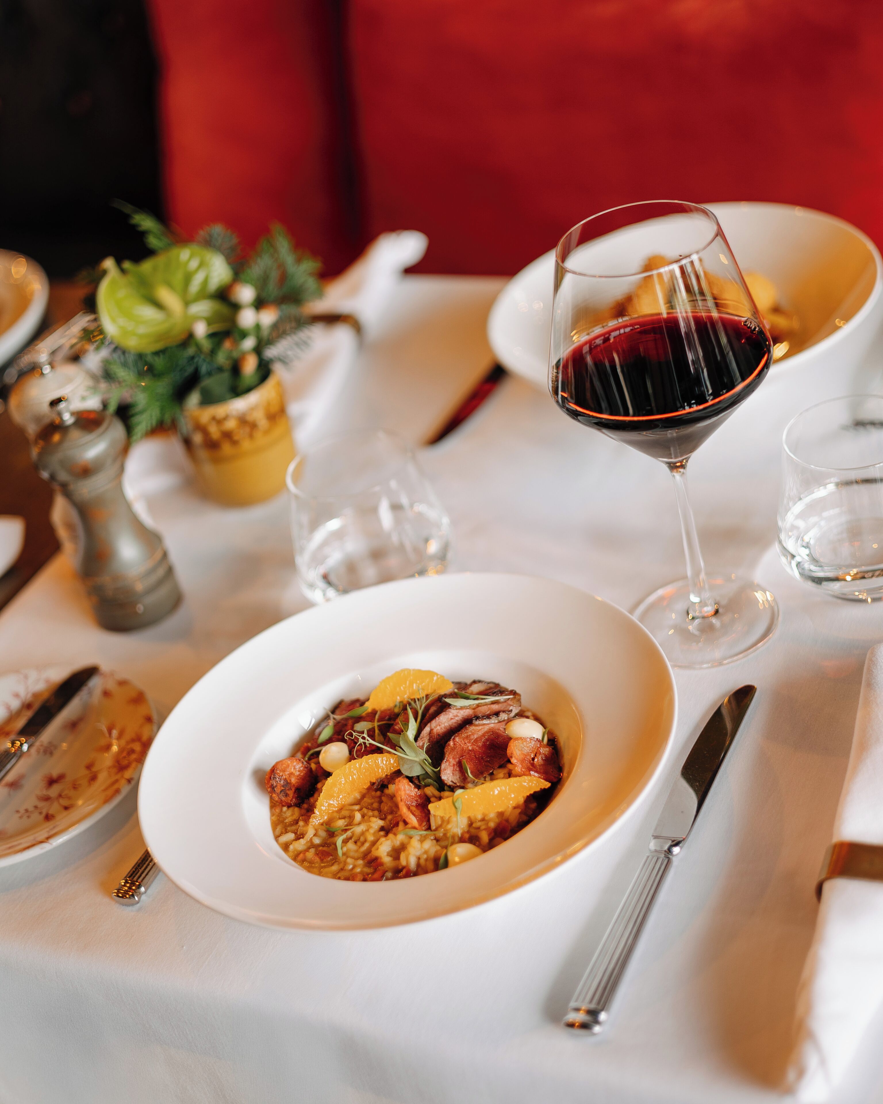 Une table à manger recouverte d’une nappe blanche, un bol rempli de nourriture, un verre de vin rouge et un salier et un poivrier.