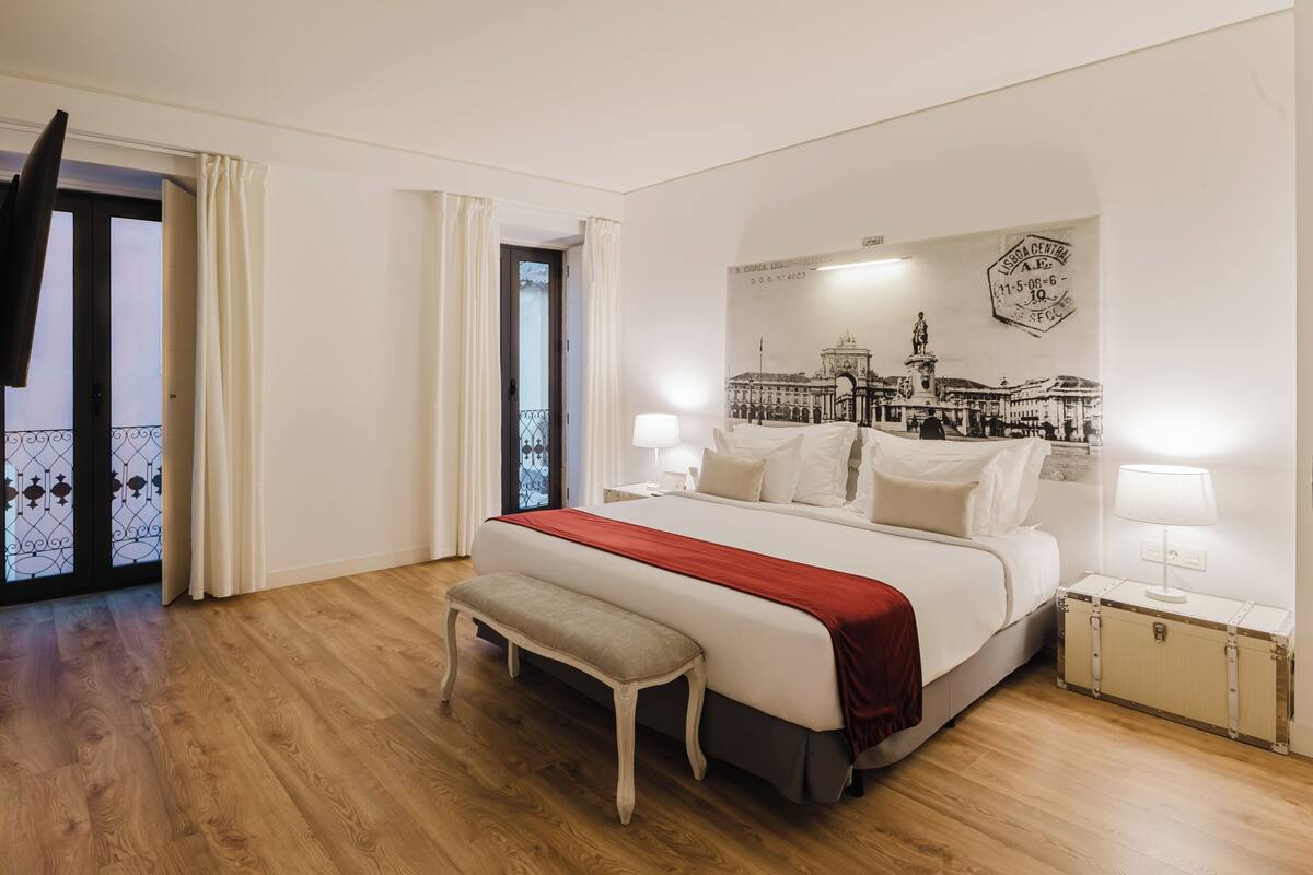 Ein Hotelzimmer mit einem großen Bett, einer Bank, einem Koffer und einer Wandlampe.