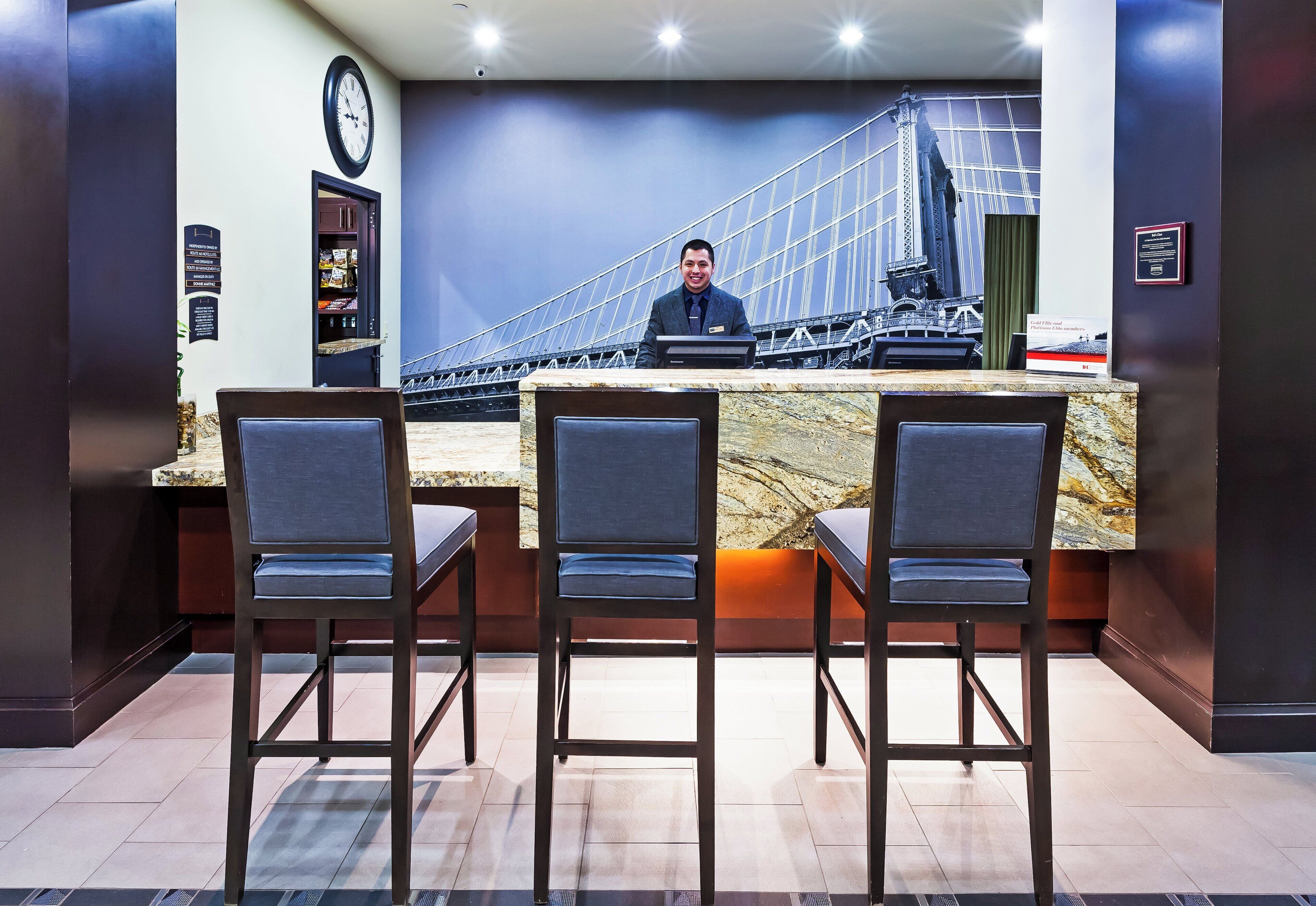 Un mostrador de recepción con vista a un puente, tres taburetes de bar, un reloj y un cartel.
