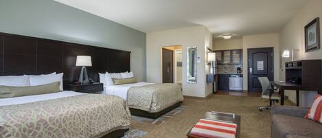 A hotel room with two beds, a kitchenette, a dining area, and a living room with a sofa and ottoman.