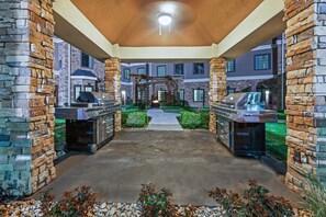 Un patio al aire libre con pilares de piedra, una pérgola y dos parrillas para barbacoa.