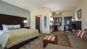 Habitación de hotel con una cama grande, un sofá, una mesita, una kitchenette y un televisor.