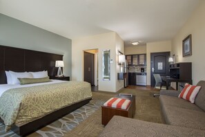 Habitación de hotel con una cama grande, un sofá, una mesita, una kitchenette y un televisor.