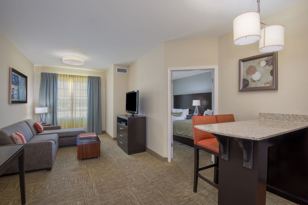 A hotel room with a sofa, a small desk, a TV, a bed, and a dining area.
