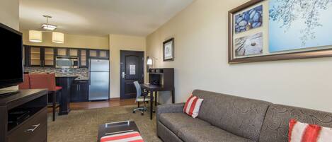 A compact living space with a kitchenette, a sofa, a television, and a framed artwork on the wall.