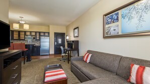 Un espacio habitable compacto con kitchenette, un sofá, un televisor y un cuadro en la pared.