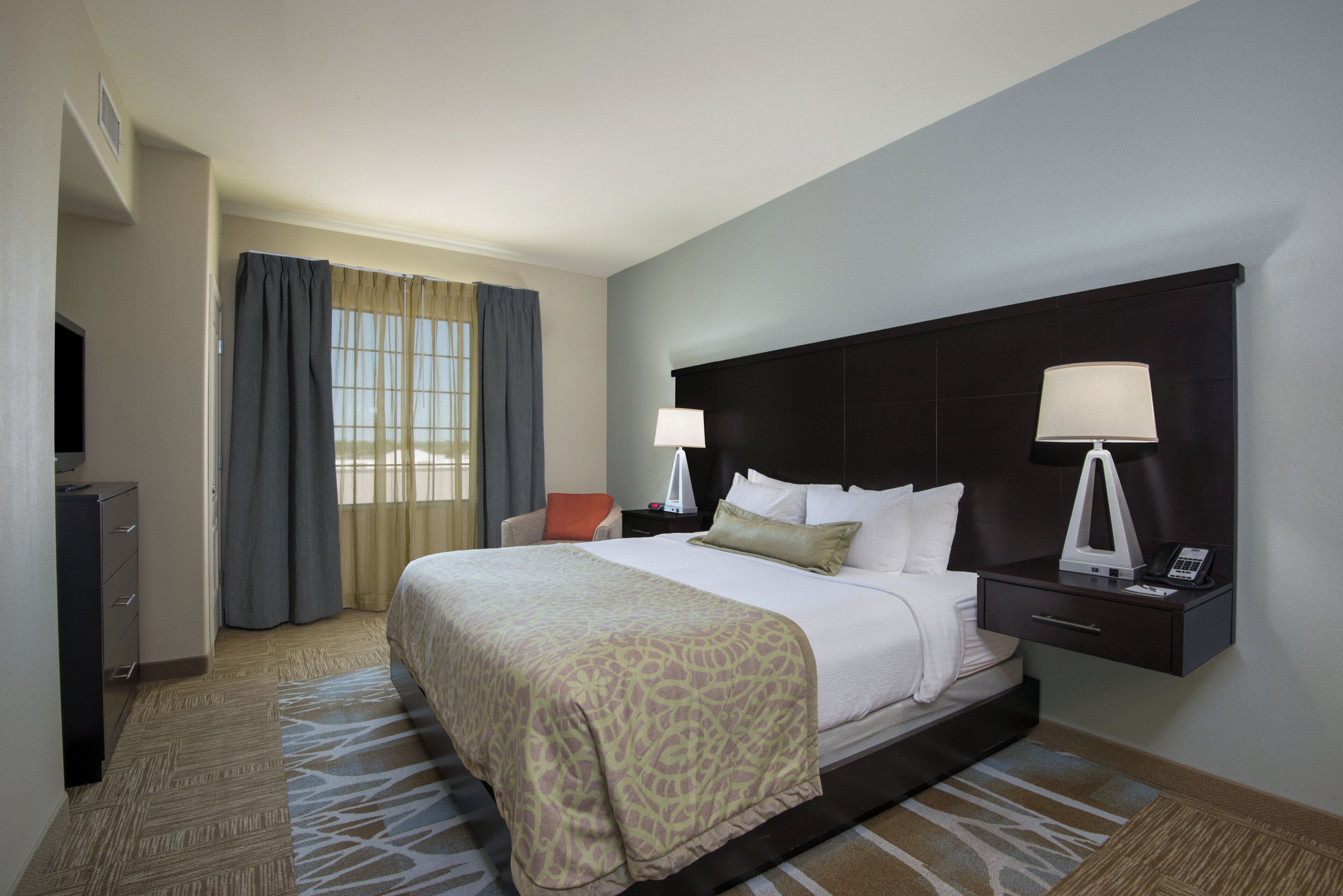 Quarto de hotel com uma cama grande, duas luminárias de cabeceira, uma escrivaninha com telefone e uma cadeira.