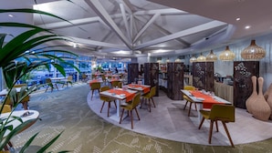 A modern restaurant with a high ceiling, large windows, and a view of the city. Tables are arranged in a semi-circular pattern, and there are large decorative vases on the walls. - Garrigae Domaine de l'Esterel (Saint-Raphael)