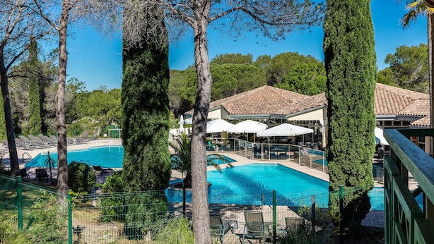 A pool area with lounge chairs and umbrellas, surrounded by trees and a building with a tiled roof. - Garrigae Domaine de l'Esterel (Saint-Raphael)