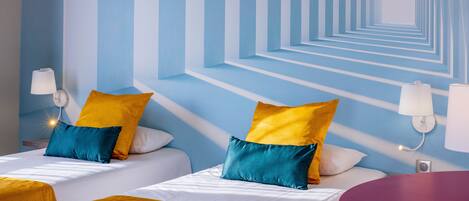 A hotel room with two beds, each with yellow and blue pillows, a red table, and a patterned wall.