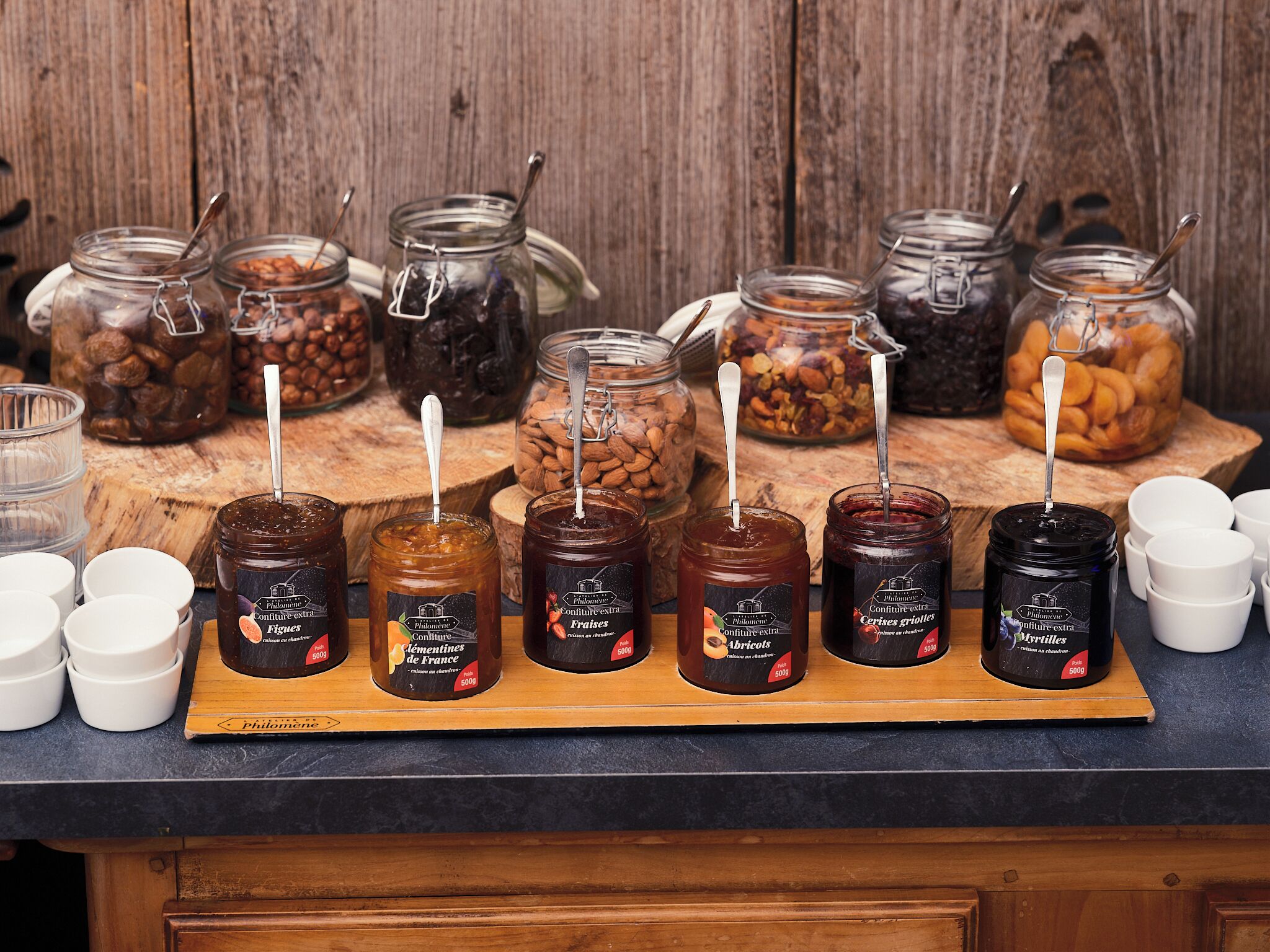 A wooden table with jars of preserves and a wooden board with jars of jam.
