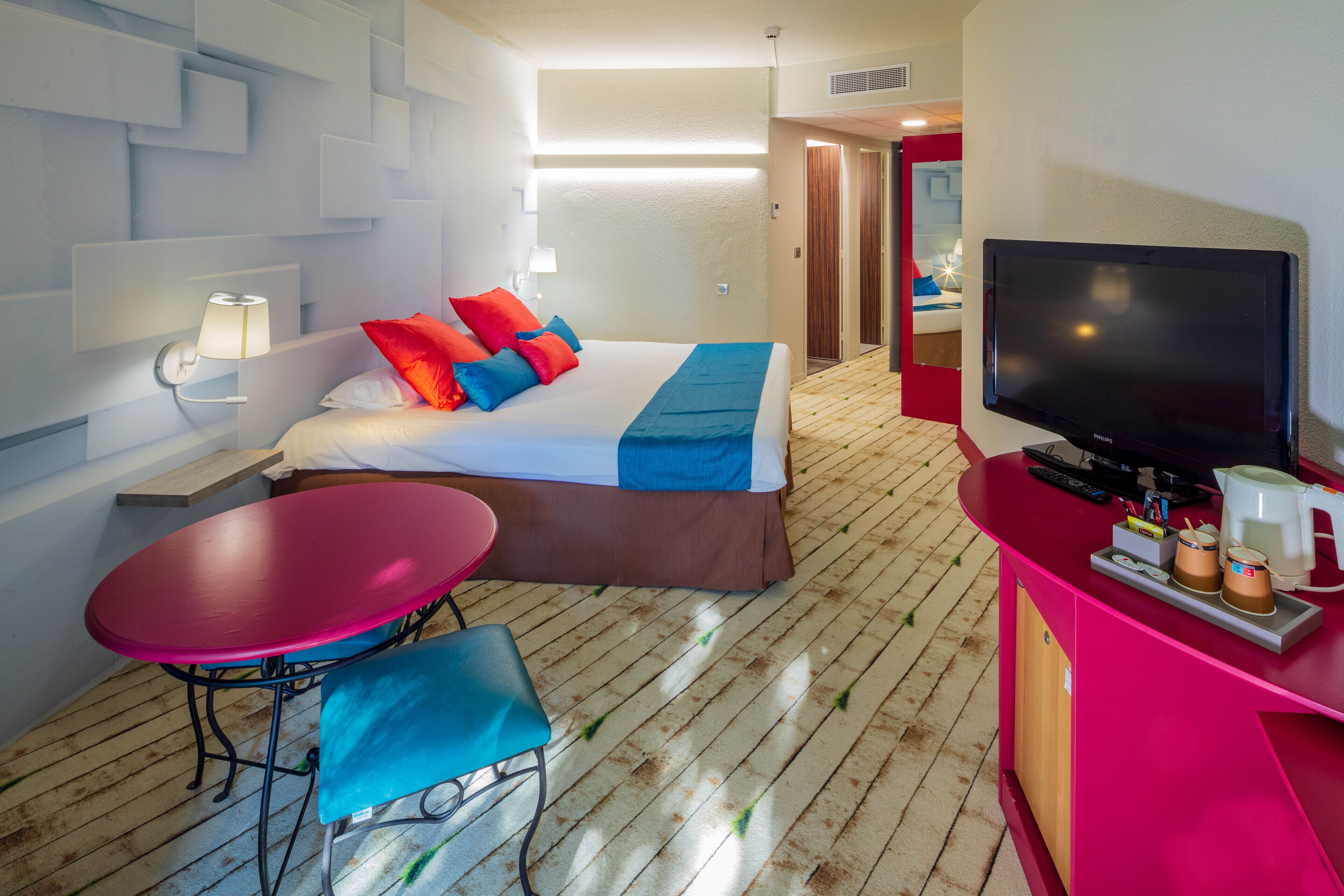 A hotel room with a bed, a TV, a desk, and a table.