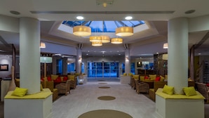 A spacious lobby with a central walkway, seating areas with yellow cushions, and a skylight above. - Garrigae Domaine de l'Esterel (Saint-Raphael)