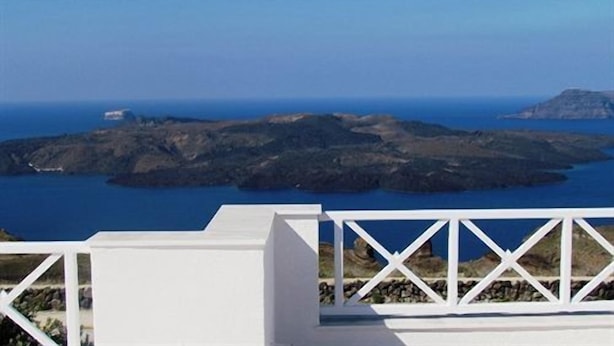 A white building with a white balcony overlooking a coastal landscape with rocky terrain and the sea.