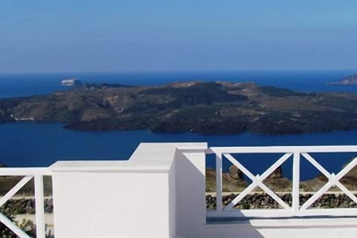 Un bâtiment blanc doté d’un balcon blanc, surplombant un paysage côtier caractérisé par un terrain rocheux et la mer.