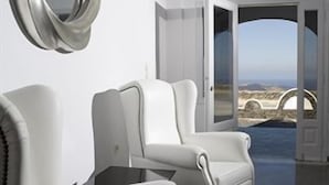 A modern room with two white leather armchairs, a large mirror, and a view of the sea through an open door.