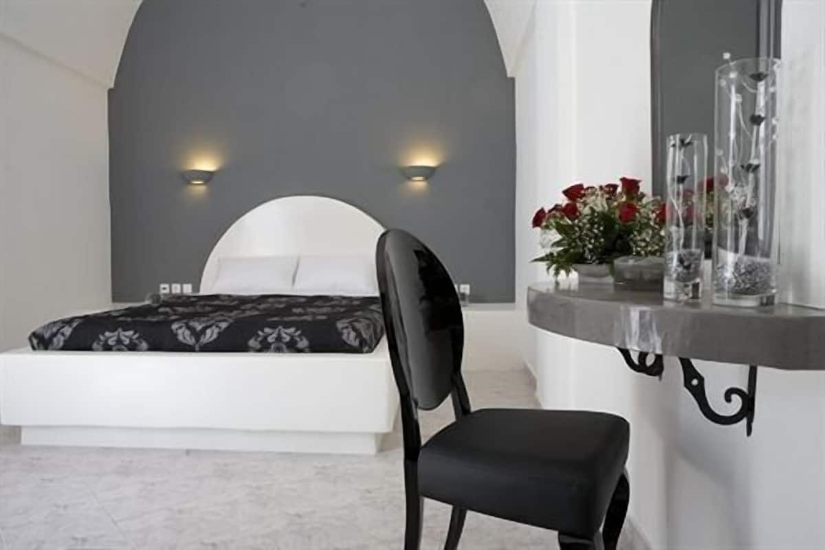 Une chambre moderne avec un grand lit, une chaise noire, une table de chevet ornée d’un vase de fleurs et deux lampes fixées au mur.