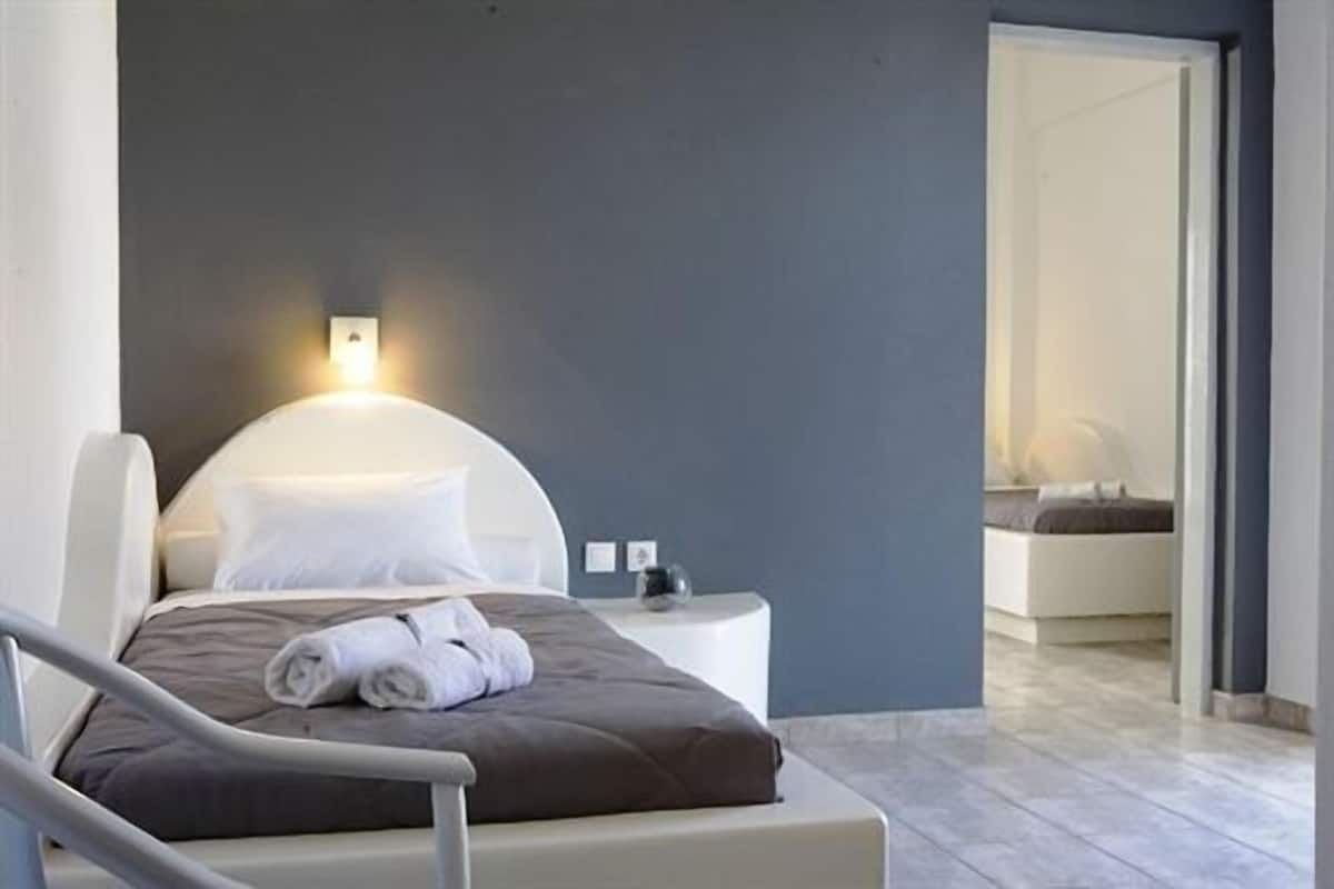 Une chambre d’hôtel moderne, équipée d’un lit, d’une table de chevet et d’une salle de bain visible à travers une porte ouverte.