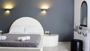 A modern bedroom with a curved ceiling, a bed with white bedding, a round bedside table, and a black trash bin.