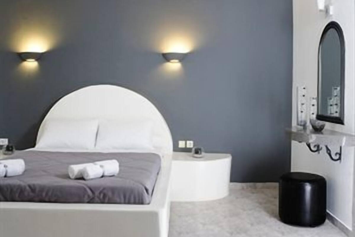 Une chambre à coucher moderne avec un plafond incurvé, un lit avec une literie blanche, une table de chevet ronde et une poubelle noire.