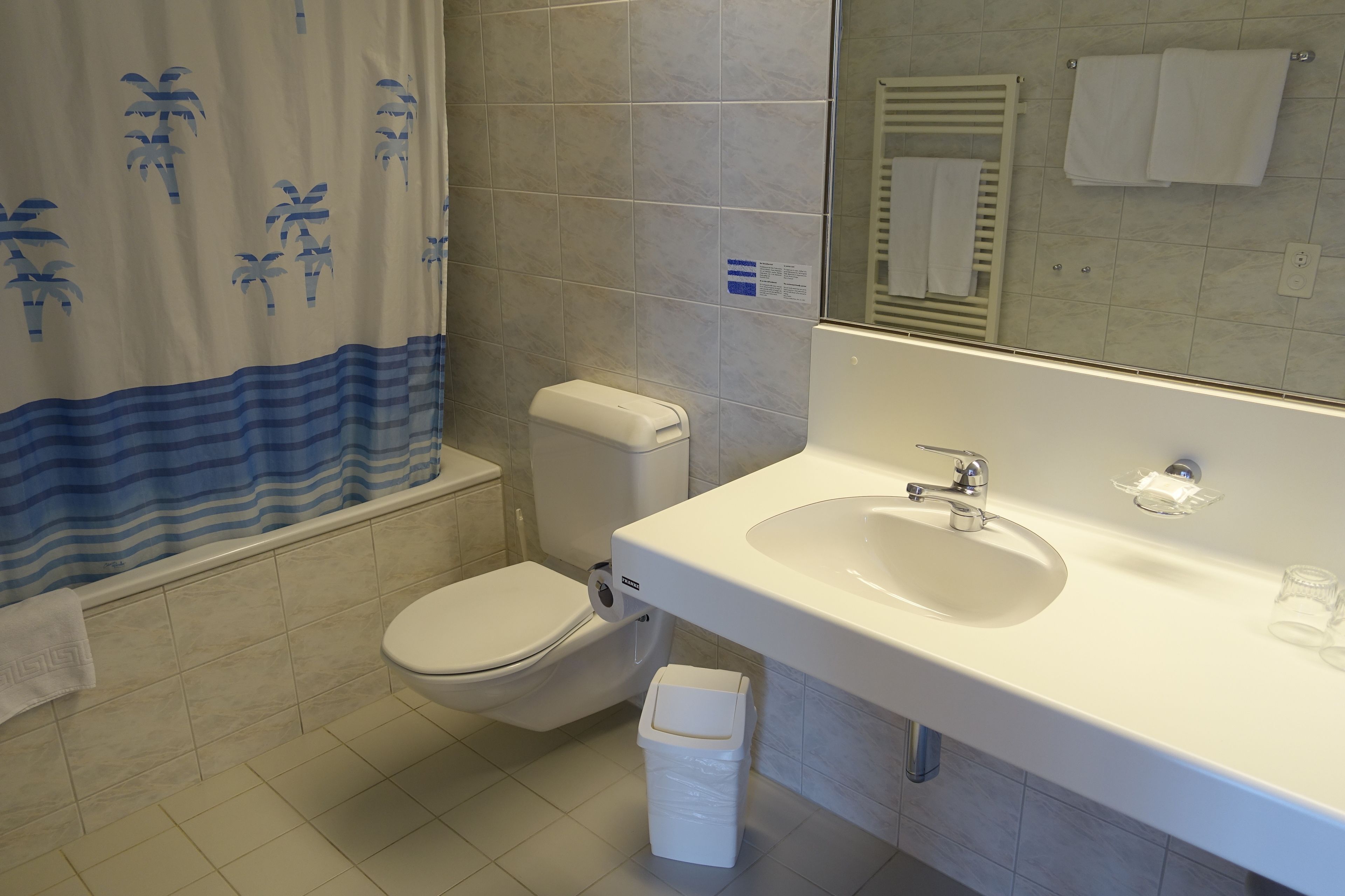 Baño con inodoro, lavamanos y cortina de ducha con diseño de palmera.