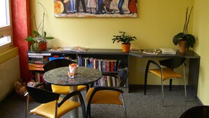 A cozy reading area with a round table, yellow chairs, a bookshelf, and a painting on the wall. - Hotel Schweizerhof Engelberg (Engelberg)