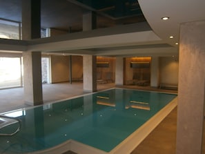 A modern indoor swimming pool with clear water, surrounded by a spacious area with seating and a high ceiling. - Hotel Zum Löwen - Al Leone (Meltina)