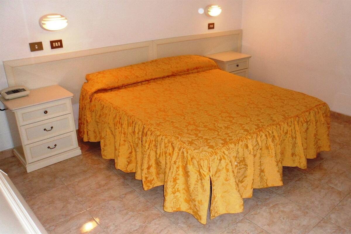 A bedroom with a bed, a nightstand, a chair, and a wall-mounted light fixture.