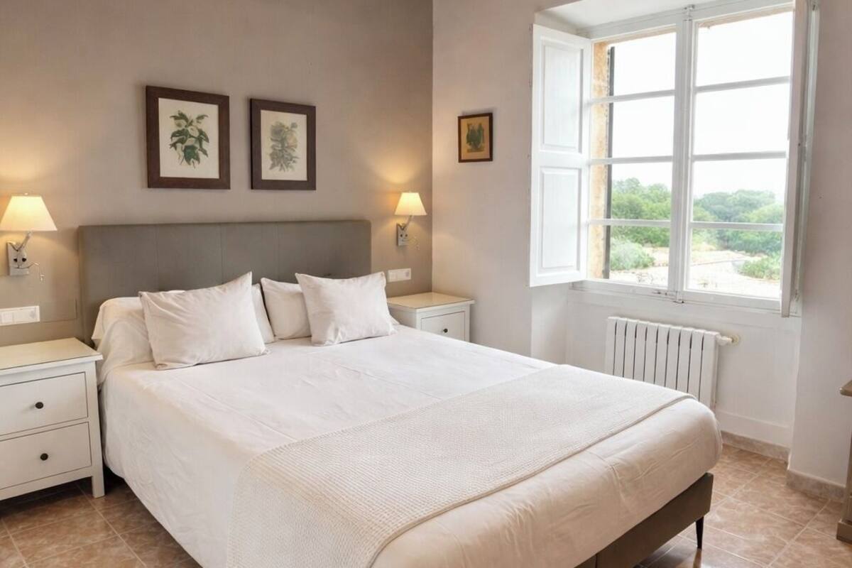 A bedroom with a bed, nightstands, a window, and wooden ceiling beams.