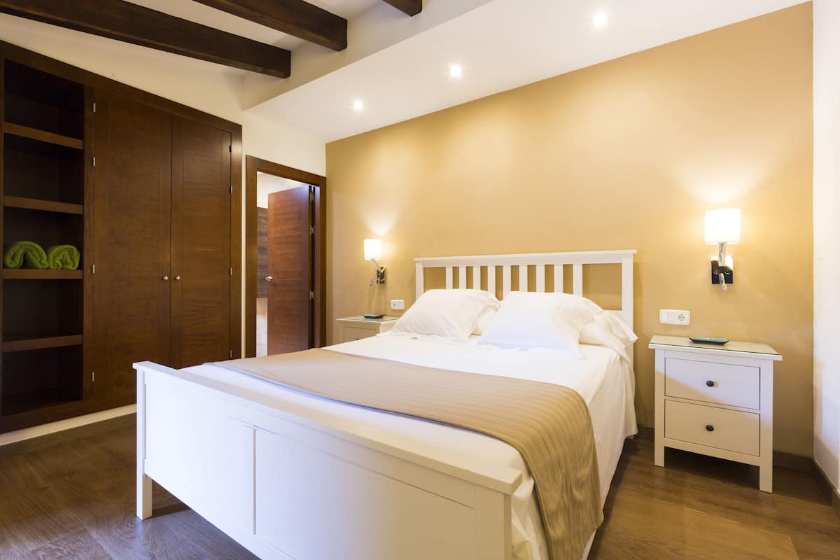 A bedroom with a bed, nightstands, a wardrobe, and a wall-mounted light fixture.