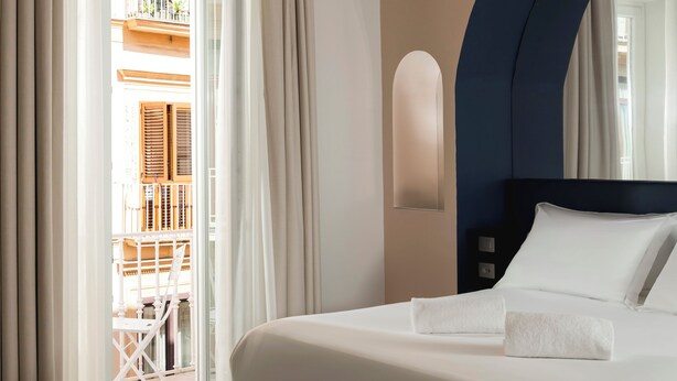 A hotel room with a bed, curtains, a chair, and a view of an outdoor balcony. - Palazzo Tasso (Sorrento)