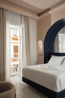 Habitación de hotel con cama, cortinas, una silla y vistas a un balcón exterior.