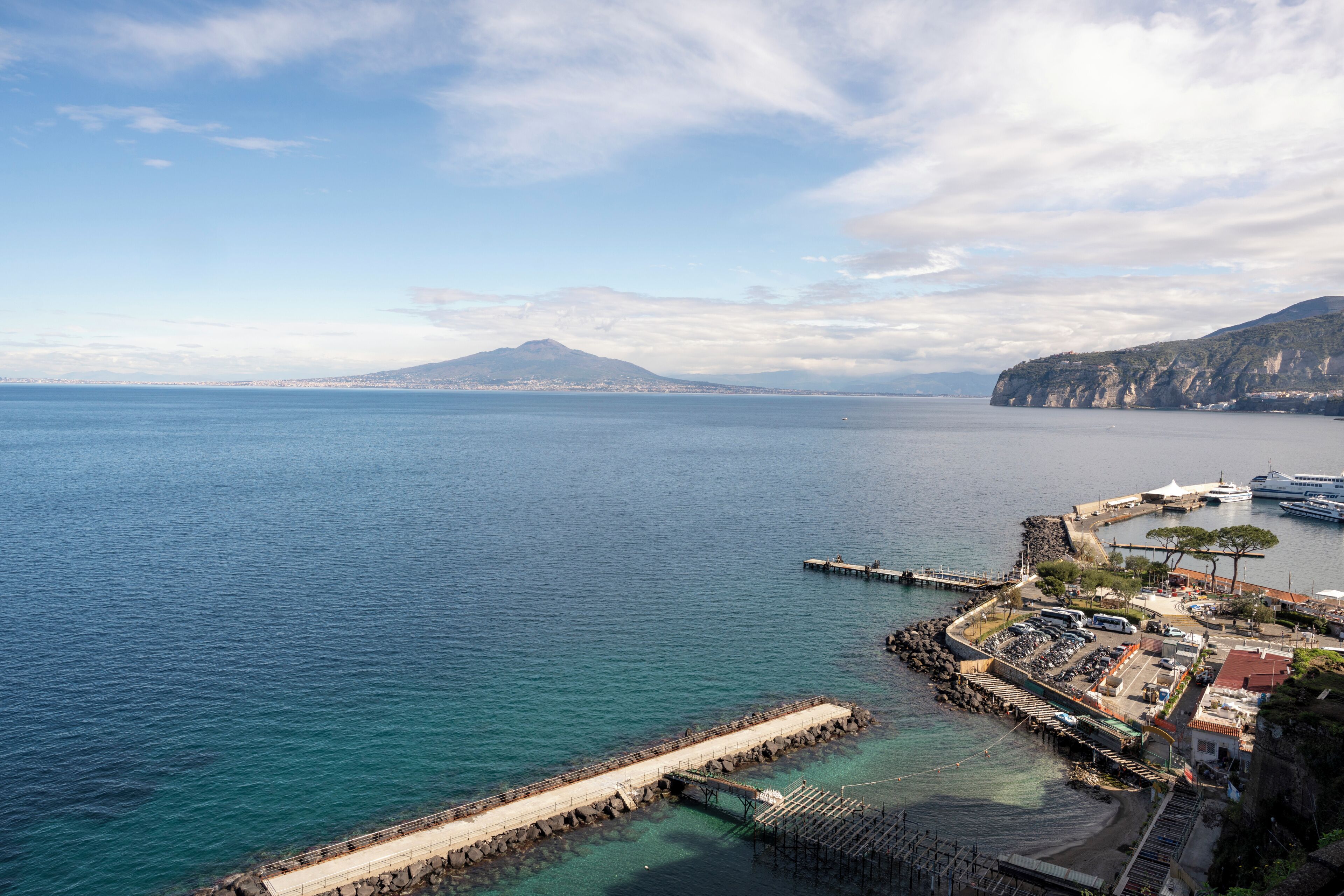 A coastal town with a pier, a mountain in the background, and a clear sky.