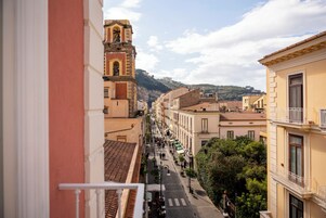 Vista de la calle con edificios, una torre campanario y una montaña al fondo.