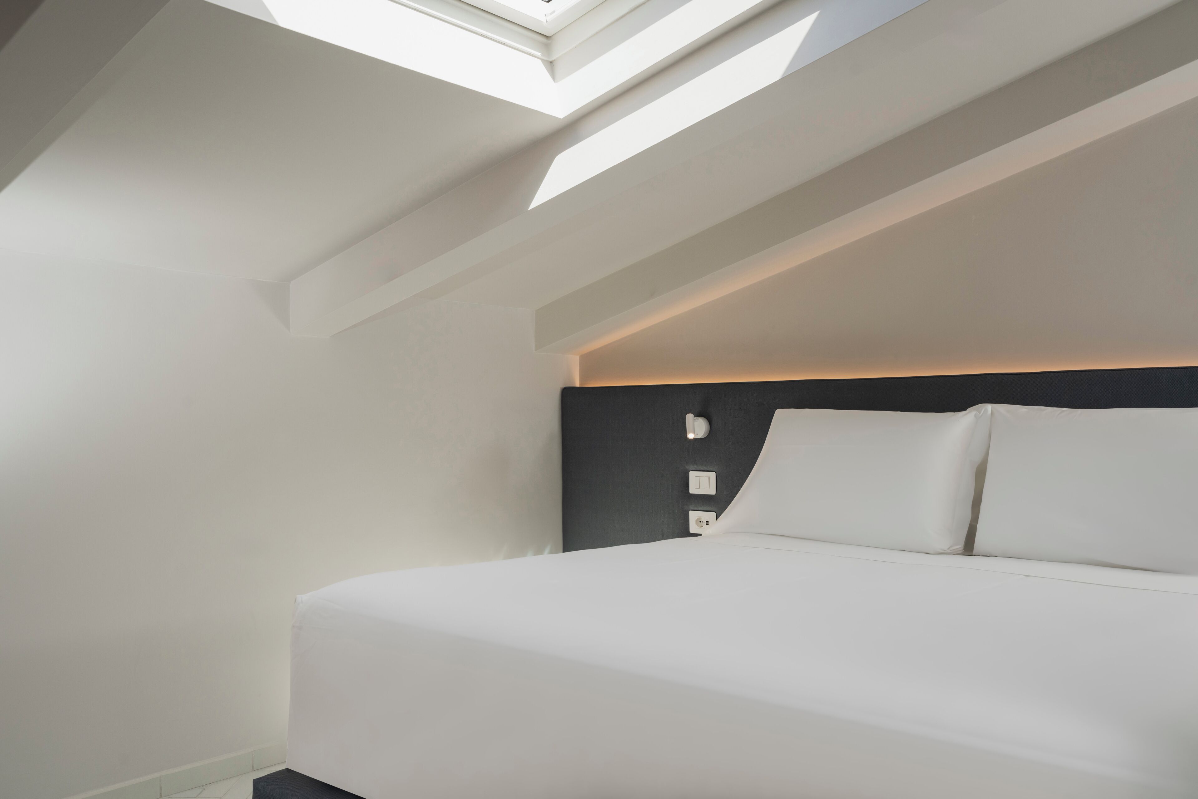 A modern bedroom with a skylight, a bed, and a dark headboard.