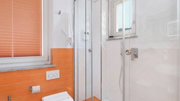 Une salle de bain avec une douche à parois de verre, un lavabo blanc et des murs recouverts de carreaux orange.