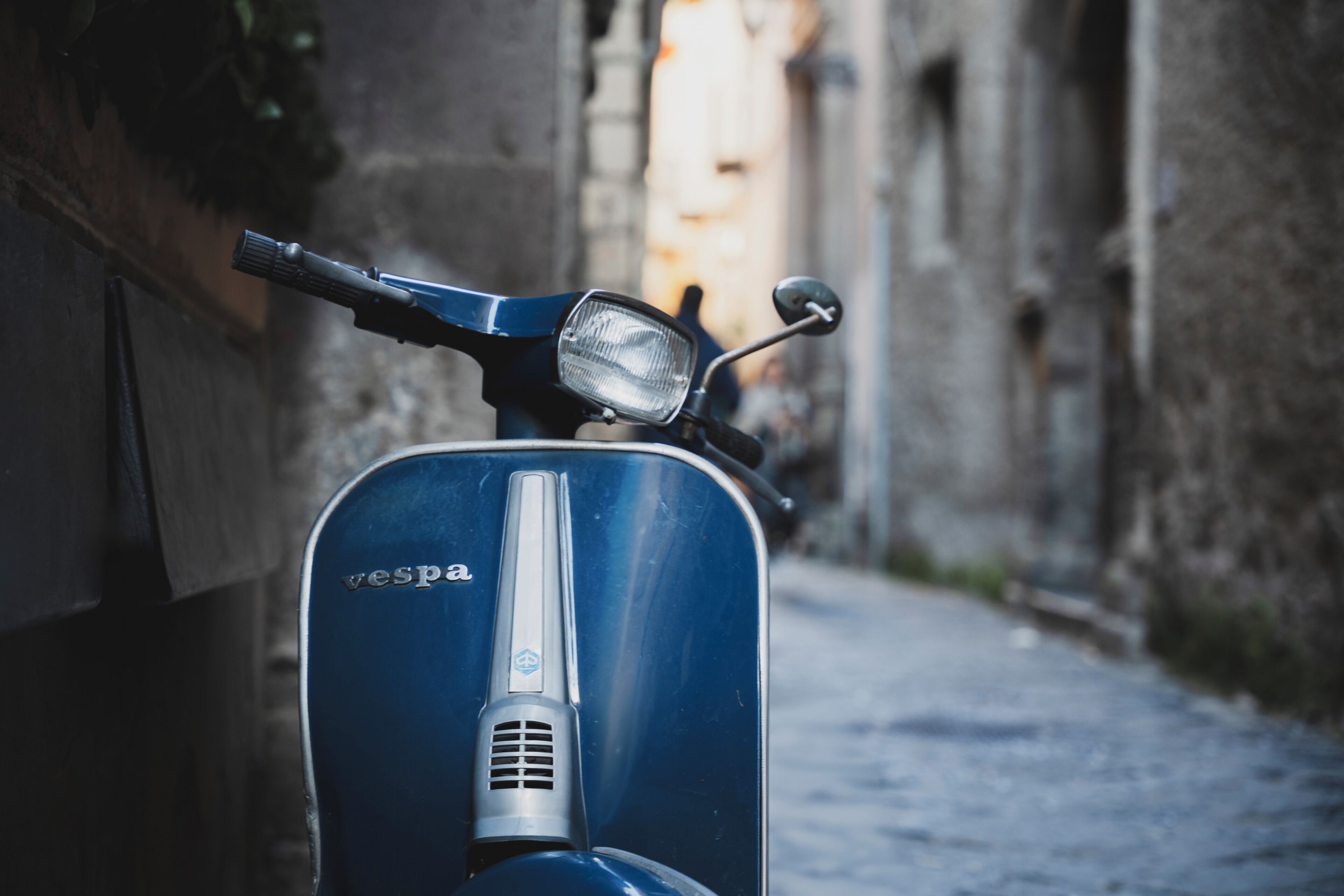 A blue Vespa parked on a cobblestone street.