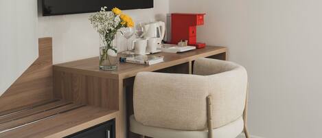 A modern room with a wooden desk, a chair, a TV, a coffee maker, and a small plant.